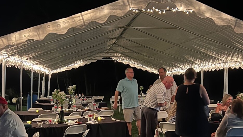 20x40 white event tent at night illuminated by bistro string lights, with guests at tables underneath